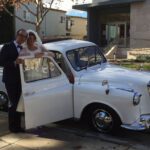 Couple posing at front passenger door of white '92 London Taxi