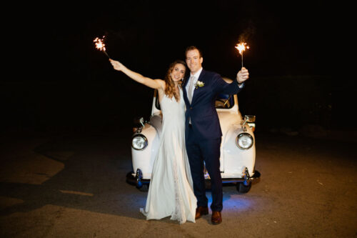 Smiling newlyweds holding sparklers in front of London taxi