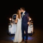 Newlyweds kissing in front of London taxi carriage holding sparklers at night