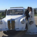Newlyweds standing outside drivers door of white '92 taxi, holding each other