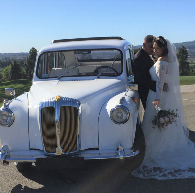 Newlyweds standing outside drivers door of white '92 taxi, holding each other