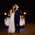 Newlyweds looking at each other touching noses holding sparklers in front of London taxi at night