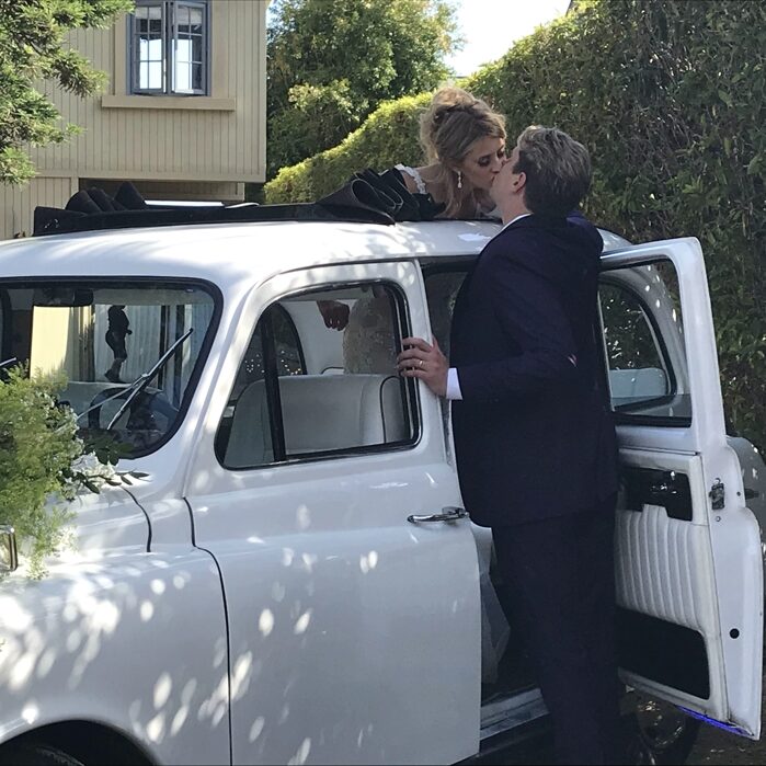Bride standing inside white '92 taxi and leaning over to kiss groom