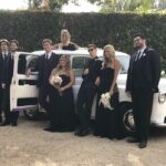 Entire wedding party posing next to white '92 London Taxi