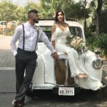 Bride seated on hood of '92 white Taxi with groom next to her