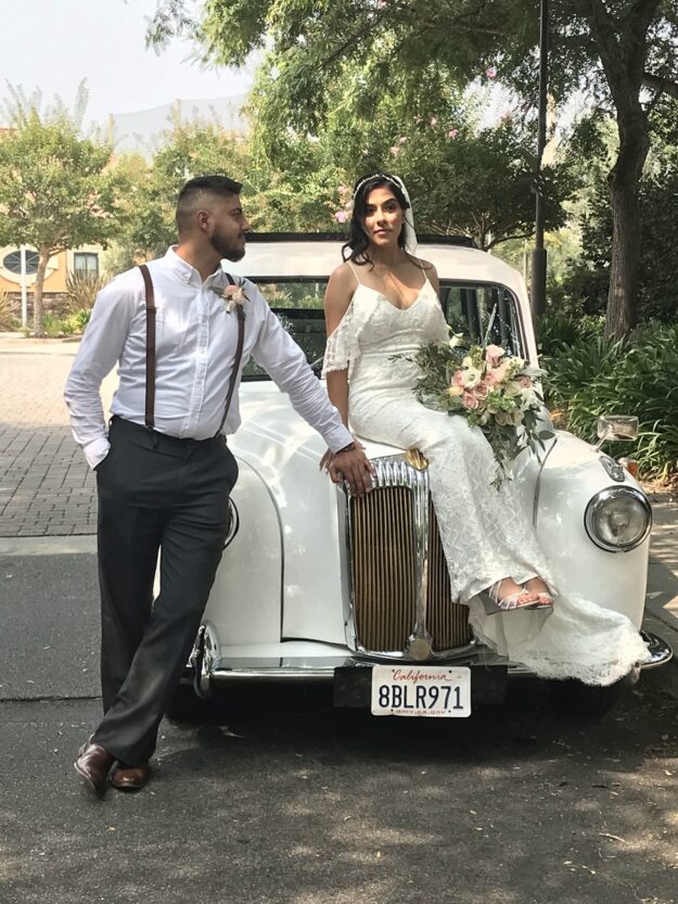 Bride seated on hood of '92 white Taxi with groom next to her