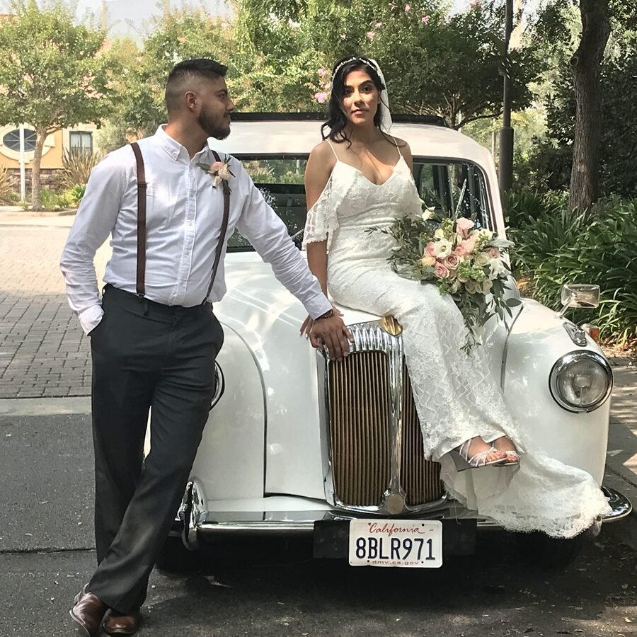Bride seated on hood of '92 white Taxi with groom next to her
