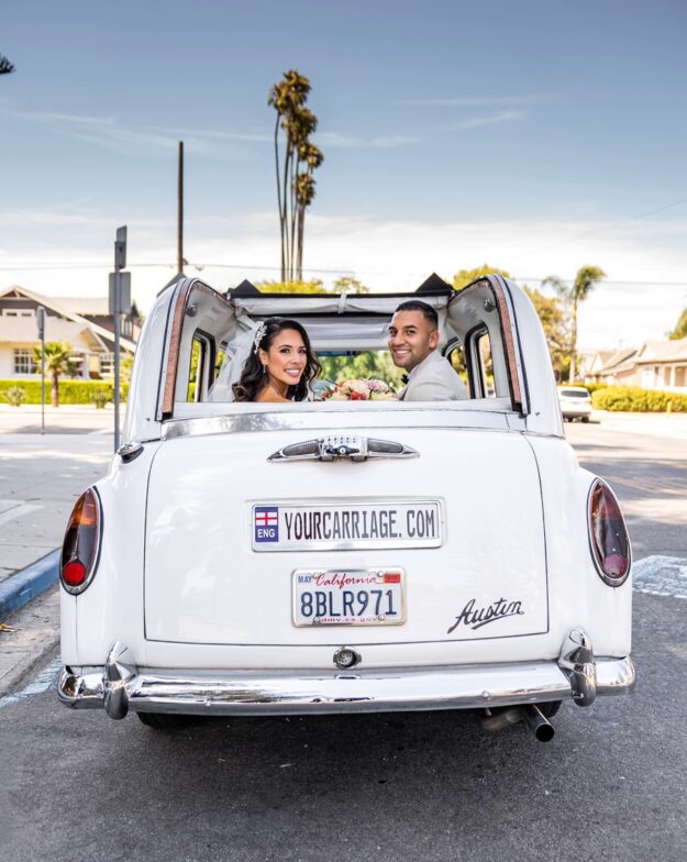 Newlyweds in back seat of Taxi car with convertible top open looking back into the camera with big smiles