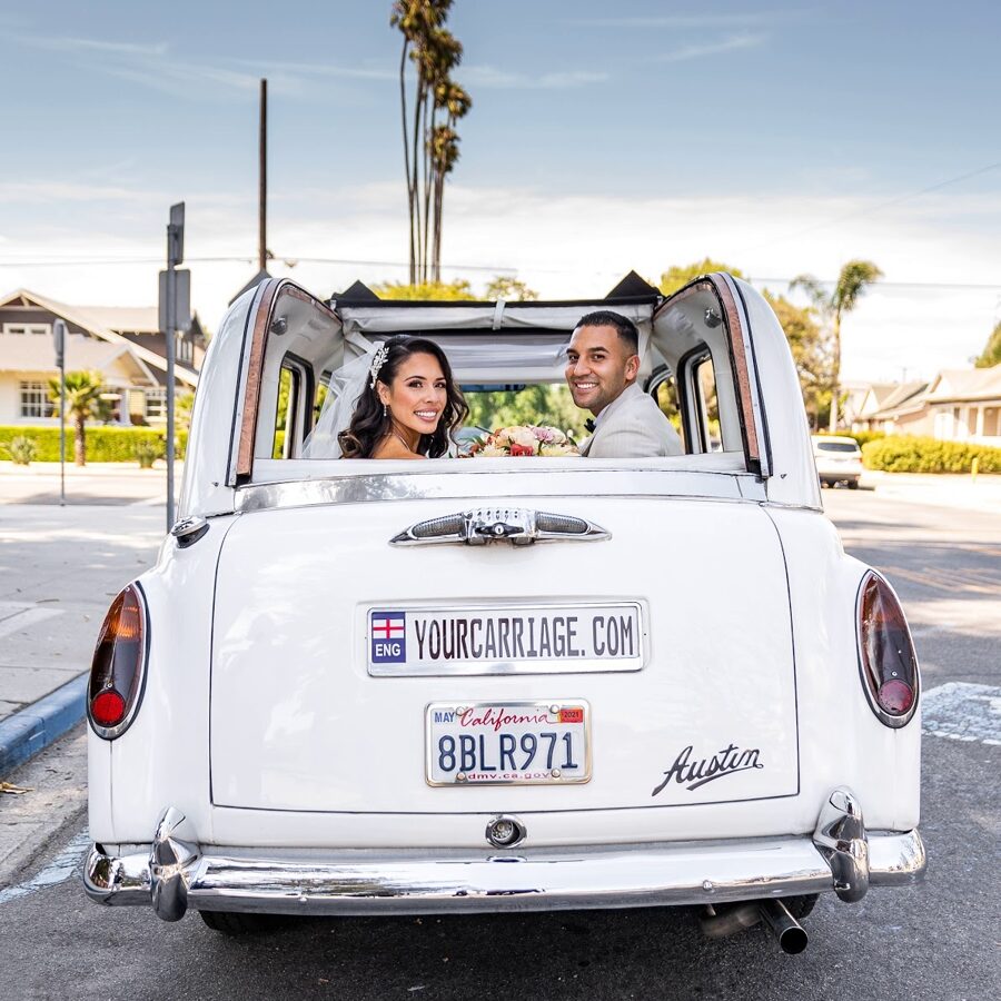 Newlyweds in back seat of Taxi car with convertible top open looking back into the camera with big smiles
