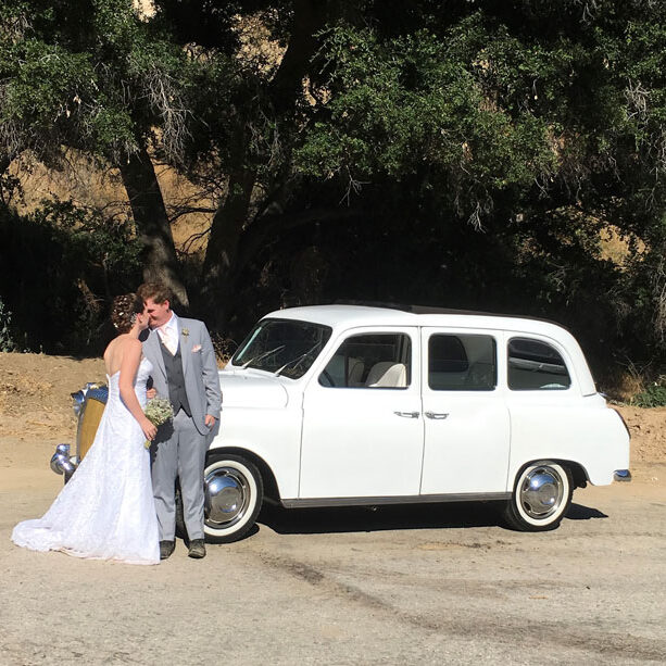 Newly wedded couple standing in front of a car.