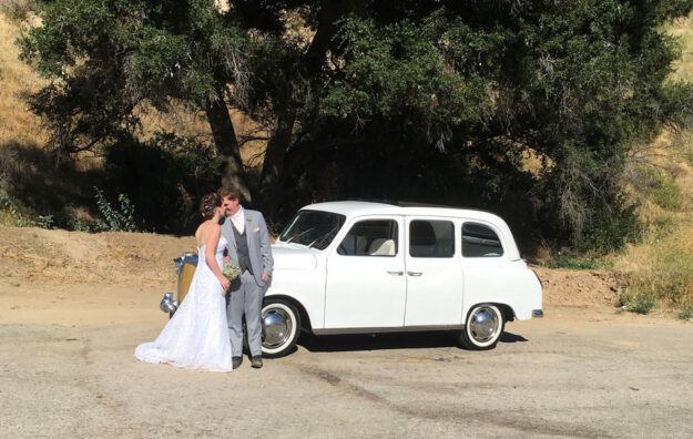 Newly wedded couple standing in front of a car.