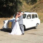 Wedding couple holding each other in front of a London Taxi cab.