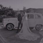 Black and white picture of a wedding couple in front of a car.