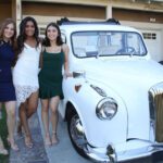 Young girls taking a picture next to a London Taxi cab.